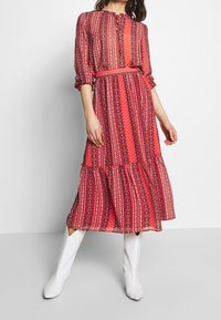 Rotes gemustertes Kleid mit langen Ärmeln, geraffter Taille und gestuftem Rock. Hergestellt aus leichtem Stoff und mit komplexen geometrischen Designs.