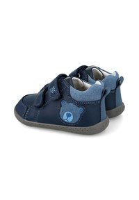 Zapatos de cuero azul marino con correas de Velcro, motivo de oso, suela de goma gris y superficies lisas y texturizadas; diseño de tobillo bajo.