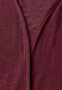 Burgundy stickad tyg med en subtil struktur, med en V-ringad design och kontrasterande sömdetalj. Mjukt och lätt material.