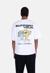 White cotton t-shirt featuring cartoon graphics of the Earth and Sun, with the text "SUPPORT YOUR Fellow Citizens." in bold black lettering.