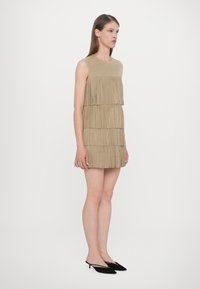 Rochie franjurată bej cu un top solid, având benzi stratificate de material. Asortată cu tocuri slingback negre. Design minimalist și textură netedă.