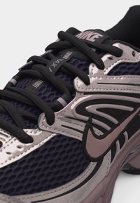 Κοντινό πλάνο αθλητικού παπουτσιού Nike Air Max που δείχνει μαύρα κορδόνια, μοβ πλέγμα στην επάνω επιφάνεια και αντανακλαστικά ασημένια επιρόδια με το λογότυπο Nike Swoosh.