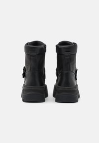Bottes à cheville en cuir noir avec semelle épaisse, dotées de fermetures éclair latérales et de détails à boucle. Texture lisse avec un design minimaliste.