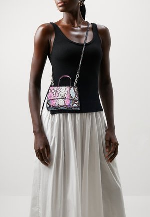 Femme portant un haut noir sans manches et une jupe plissée blanche, portant un petit sac bandoulière coloré à motif peau de serpent.