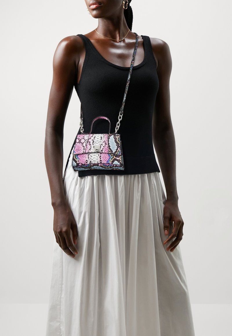 Femme portant un haut noir sans manches et une jupe plissée blanche, portant un petit sac bandoulière coloré à motif peau de serpent.
