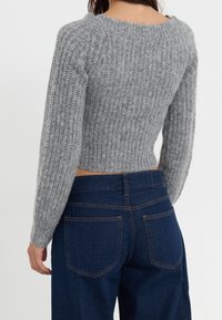 Pull gris court avec texture côtelée et manches longues ; associé à un jean taille haute bleu foncé avec poche de conception standard.
