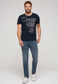 Camiseta azul marino con texto impreso, complementada por unos vaqueros azul claro y zapatillas blancas. Manga corta, cuello redondo y corte relajado.