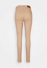 Smal jeans i en ljus beige färg. Har en slät textur, standard bakfickor och en läderliknande detalj vid midjan.