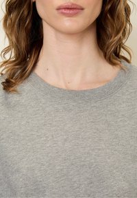 Hele halli lühikeste varrukatega sweatshirt ümmarguse kaelusega, valmistatud pehmest puuvillakangast, millel on sile tekstuur ja minimaalne õmblus.