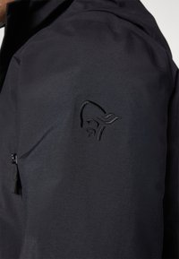 Chaqueta negra con un acabado texturizado, que presenta un bolsillo con cremallera y un sutil logo en relieve en la manga.