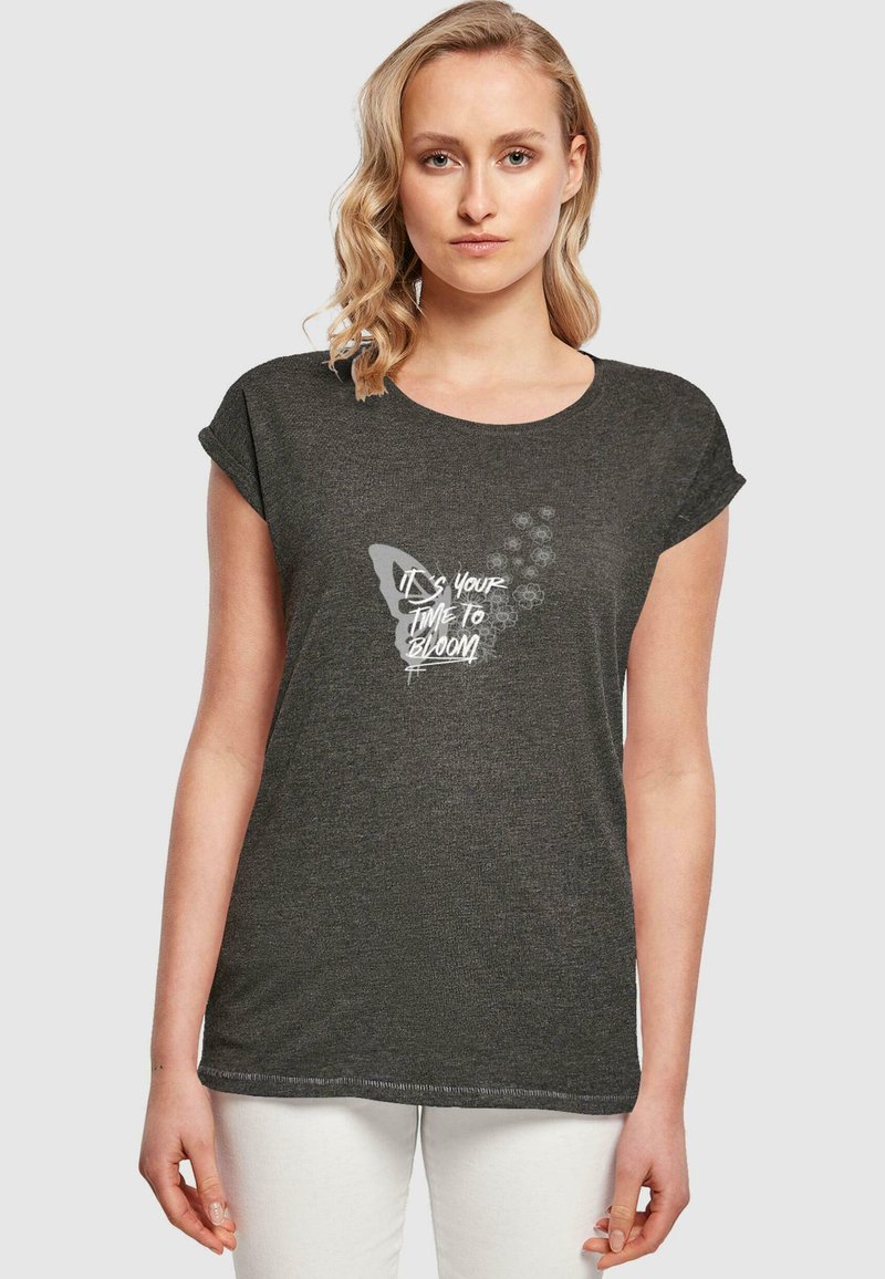 Mørkegrå kortærmet t-shirt lavet af blødt stof, med et sommerfuglegrafik og teksten "Det er din tid til at blomstre" i hvid.