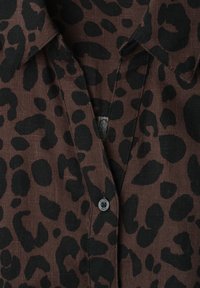 Chemise marron avec des taches léopard noires irrégulières, col chemise et un bouton visible portant la mention "street one".