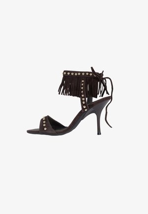 Sandale noire à talon haut avec franges à la cheville, ornements de clous dorés, bout ouvert et fermeture à nouer à l'arrière.