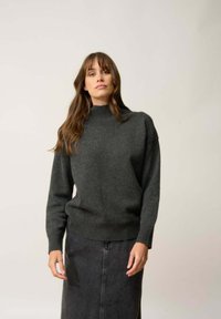 Ciemnoszary sweter wykonany na drutach z wysokim kołnierzem i prążkowanym dołem, w połączeniu z ciemną spódnicą do kolan. Miękka faktura, casualowy styl.