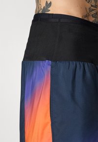 Schwarzer, strukturierter Bund über Shorts mit einem Verlauf von Dunkelblau zu Orange und Lila. Leichtes Material.