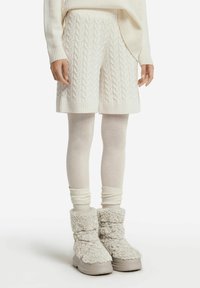 Vita kabelstickade shorts med ribbade muddar, i kombination med vita leggings och texturerade, fluffiga stövlar med tjock sula.