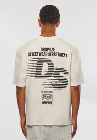Beige oversized T-shirt featuring black graphic text on back: "DROPSIZE STREETWEAR DEPARTMENT" and stylized "DS," with decorative elements.