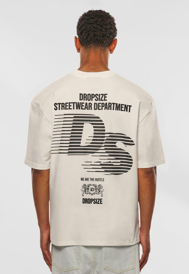 Beige oversized T-shirt featuring black graphic text on back: "DROPSIZE STREETWEAR DEPARTMENT" and stylized "DS," with decorative elements.