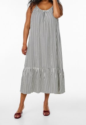Mujer que lleva un vestido midi sin mangas con rayas verticales en blanco y negro, combinado con sandalias de tacón rojas y con los dedos abiertos.