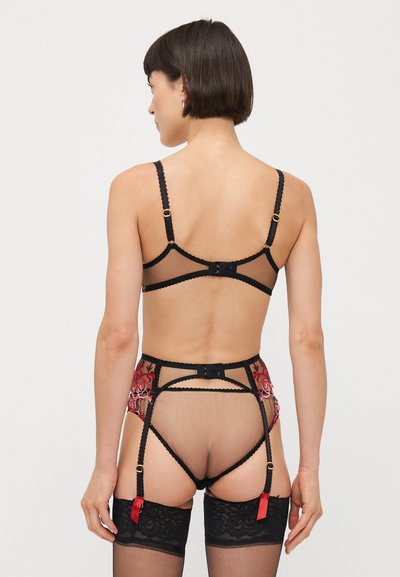 Ensemble de lingerie en dentelle noire comprenant un mesh transparent, de la broderie florale rouge, des bretelles réglables et des détails de porte-jarretelles avec des accents en ruban.
