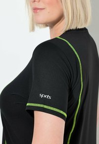 Camiseta deportiva negra con costuras verdes a lo largo de las mangas y los hombros, con el logo "sprts" en la manga izquierda en blanco.