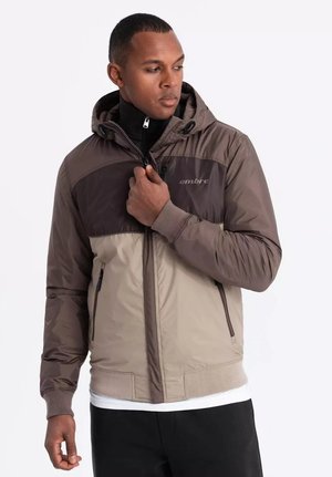 Bruin en crèmekleurige windbreakerjack met capuchon, ritsluiting, twee zakken, geribbelde manchetten en de merknaam gedrukt op de borst.