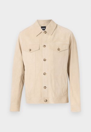 Veste en daim beige à boutons, avec deux poches poitrine à rabat et col, présentée sur un fond clair.