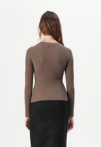 Maglione lungo a maniche ribattute di colore marrone con una silhouette aderente e collo rotondo, abbinato a una gonna nera, mostrato dal retro.