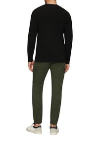 Zwarte gebreide trui met lange mouwen, gecombineerd met fitted olijfgroene joggers met elastische boorden en zijzakken, gedragen met witte sneakers.