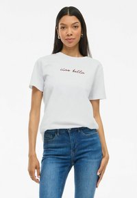 T-shirt en coton blanc à manches courtes, avec un texte en cursive rouge "ciao bella" sur la poitrine. Assorti avec un jean en denim bleu.