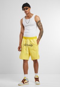 Kollane puuvillast lühike püksmeid elastse vöökoha ja paelaga, millel on mustas skripti kirjas sõna "Serenity". Kandmisel valge tank top ja sportlikud jalanõud.