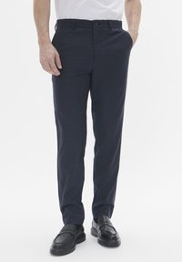 Pantalones de vestir azul marino con acabado texturizado, diseño de pierna recta y cierre de botón. Combinados con zapatos negros sin cordones.