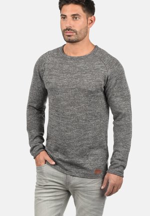 Grijze gebreide trui met lange mouwen, ronde hals en geribbelde details. Bevat een klein leren logopatch op de heup.