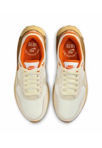 Sneakers Nike con una combinazione di colori crema e arancione, caratterizzati da una tomaia in materiali misti, sovrapposizioni testurizzate e una suola spessa e traslucida.