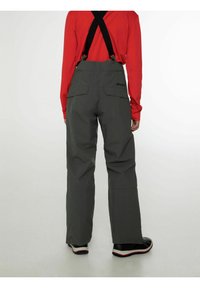 Grijze sneeuwbroek met verstelbare zwarte bretels, brede pijpen en twee achterzakken, gecombineerd met een rode longsleeve shirt.
