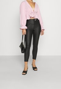 Blouse rose cintrée avec des manches bouffantes et un détail à nouer à la taille, associée à des leggings en simili cuir noir taille haute et à des mules à talons noires.