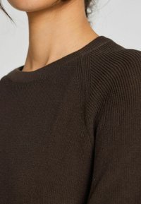 Maglione marrone lavorato a maglia con un colletto a coste e tessuto testurizzato. Presenta un design semplice e una silhouette aderente.