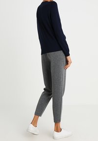 Pull en maille bleu marine associé à un pantalon de survêtement gris effilé, avec des poignets élastiques et des baskets blanches, vu de dos.