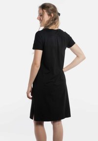 Zwart jurk met korte mouwen en een relaxed fit, voorzien van zijsplitten, zachte stof en een ronde halslijn, die de nadruk legt op een eenvoudig, modern ontwerp.
