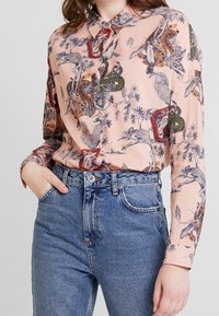 Langærmet skjorte i lyserødt stof med indviklede dyre- og plante mønstre i mørkeblå, grøn, orange og rød. Knapkrave.