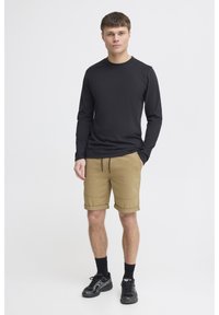 Svart långärmad skjorta, beige rullade shorts, svarta strumpor och sportskor. Enkel design, avslappnad passform, mjuk textur.
