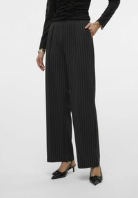 Pantalons larges à rayures noires avec une taille haute, texture de tissu lisse et une coupe décontractée, portés avec des escarpins à talons ouverts noirs.