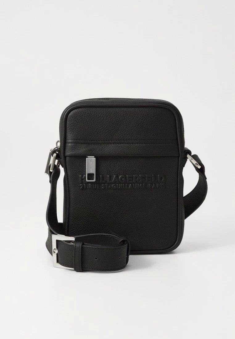 Sac bandoulière en cuir noir de forme rectangulaire, avec logo embossé, fermeture à glissière et sangle réglable. Texture lisse avec une quincaillerie minimale.