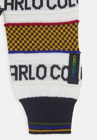 Knitted sweater in white, red, yellow, and navy. Features geometric patterns with bold black "CARLO COLUCCI" logo. Multicolored striped hem.