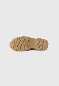 Tan rubberen zool met een gestructureerd, gegroefd patroon voor grip. Bevat het opgedrukte merk en model details op een glad oppervlak.
