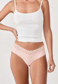 Culotte rose avec des bords en dentelle, dotée d'une partie inférieure lisse. Accompagnée d'un débardeur blanc avec un motif texturé et des bords festonnés.