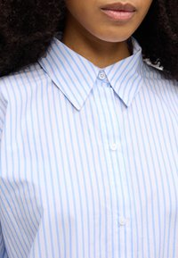 Γαλάζιο πουκάμισο με ρίγες και γιακά με κουμπιά, με λεία υφή υφάσματος και διακριτικές κάθετες ρίγες. Ορατές λεπτομέρειες με κουμπιά.