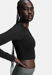 Langärmliges schwarzes Crop-Top mit glatter Textur. Kombiniert mit hochsitzzenden grauen Leggings, die eine figurbetonte Silhouette und einen sportlichen Stil zur Schau stellen.