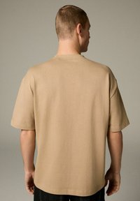 Camiseta de manga corta beige hecha de una tela suave, con un corte holgado, escote redondo y detalles de costura limpios.