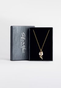 Guld kæde med et tulipanformet vedhæng, der har en glat hvid sten og funklende detaljer. Præsenteret i en sort fløjlæske.